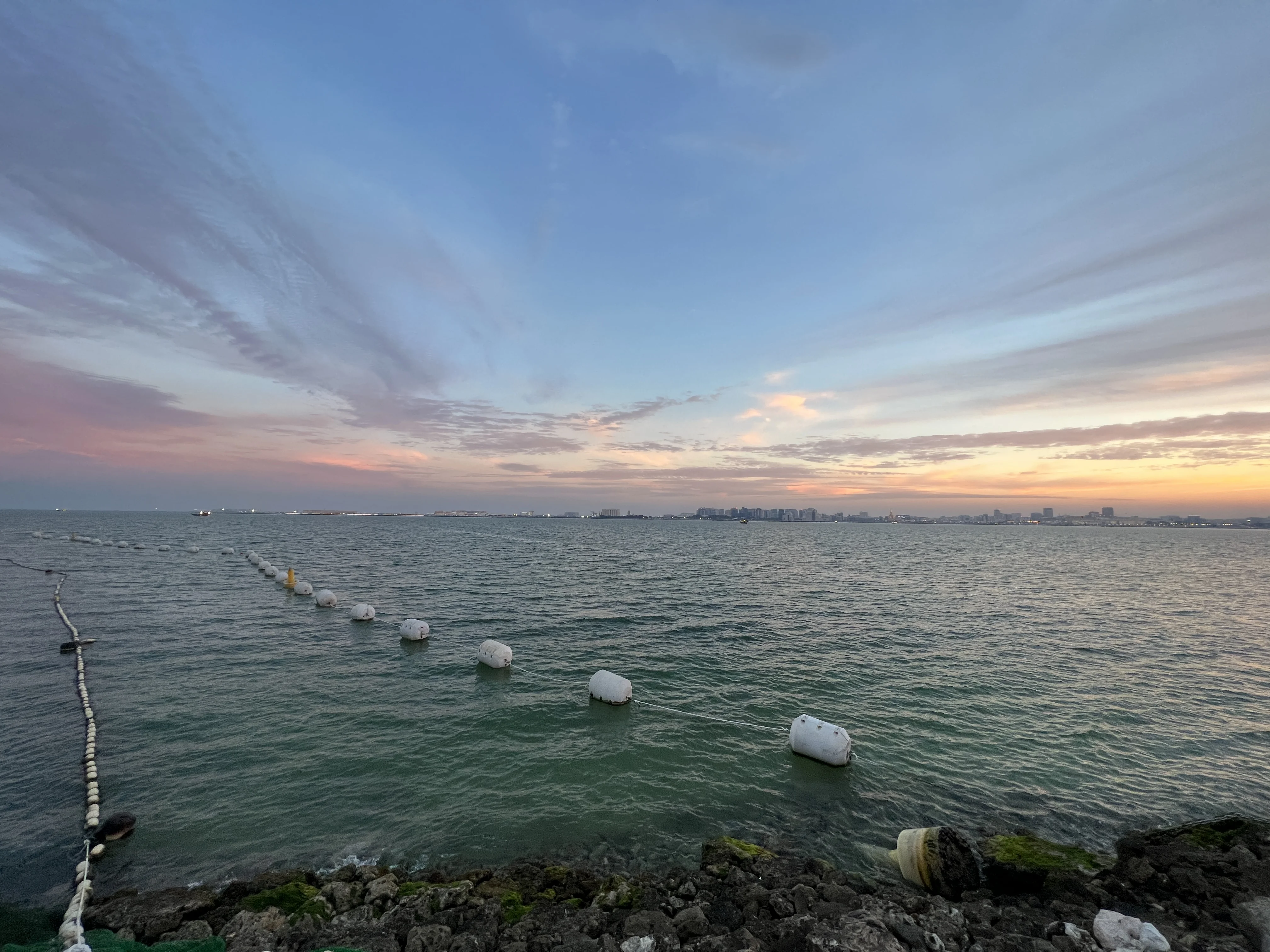 Calm Doha Bay water at twilight with West Bay towers on the horizon