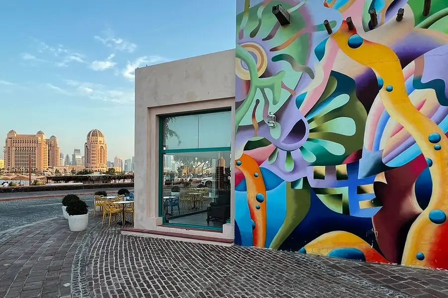 Colourful mural wall beside a waterfront restaurant at Katara Cultural Village with the Doha skyline behind