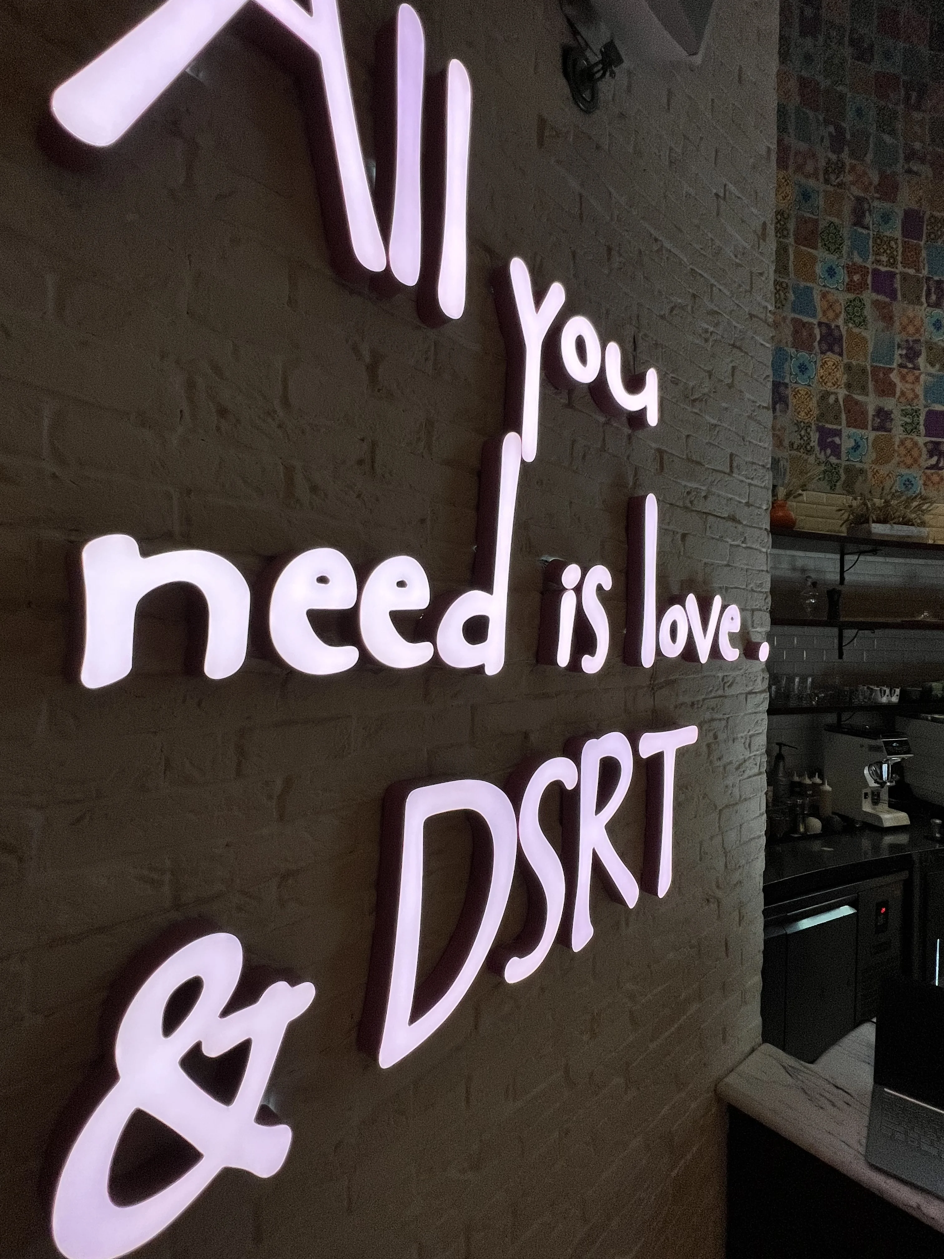 'All you need is love and DSRT' neon sign on a textured wall at Boho Social, Doha