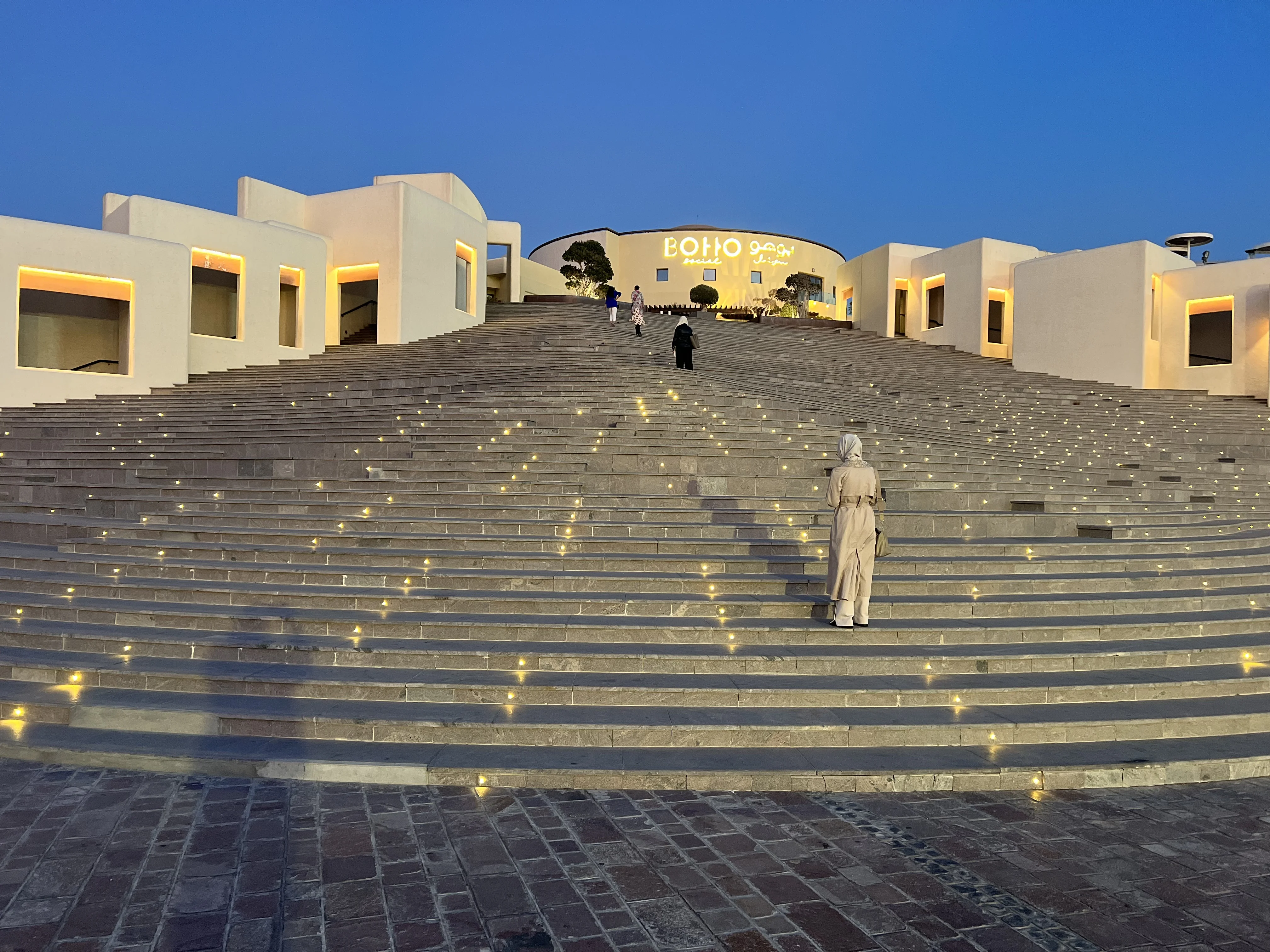 Person walking down the illuminated steps of Katara Amphitheatre at night
