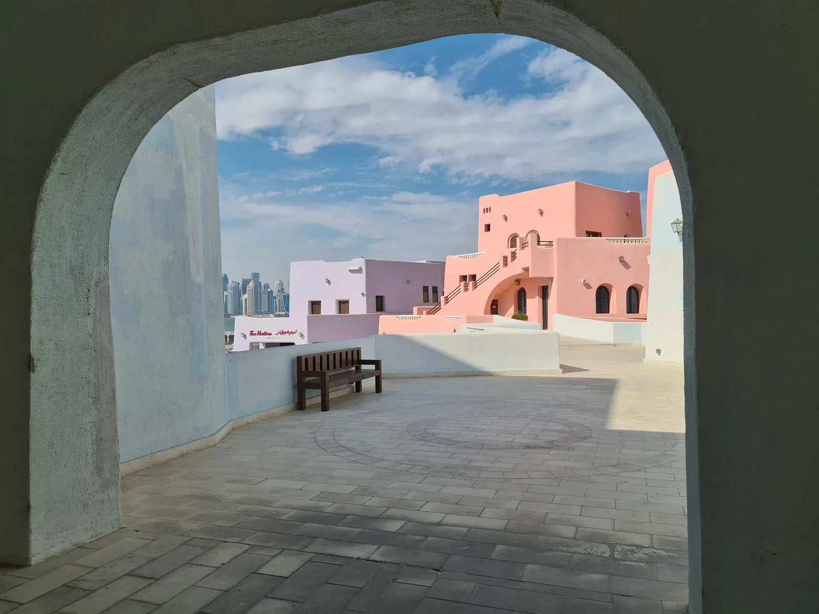 Stone archway framing pastel-coloured buildings in the Mina District, Doha