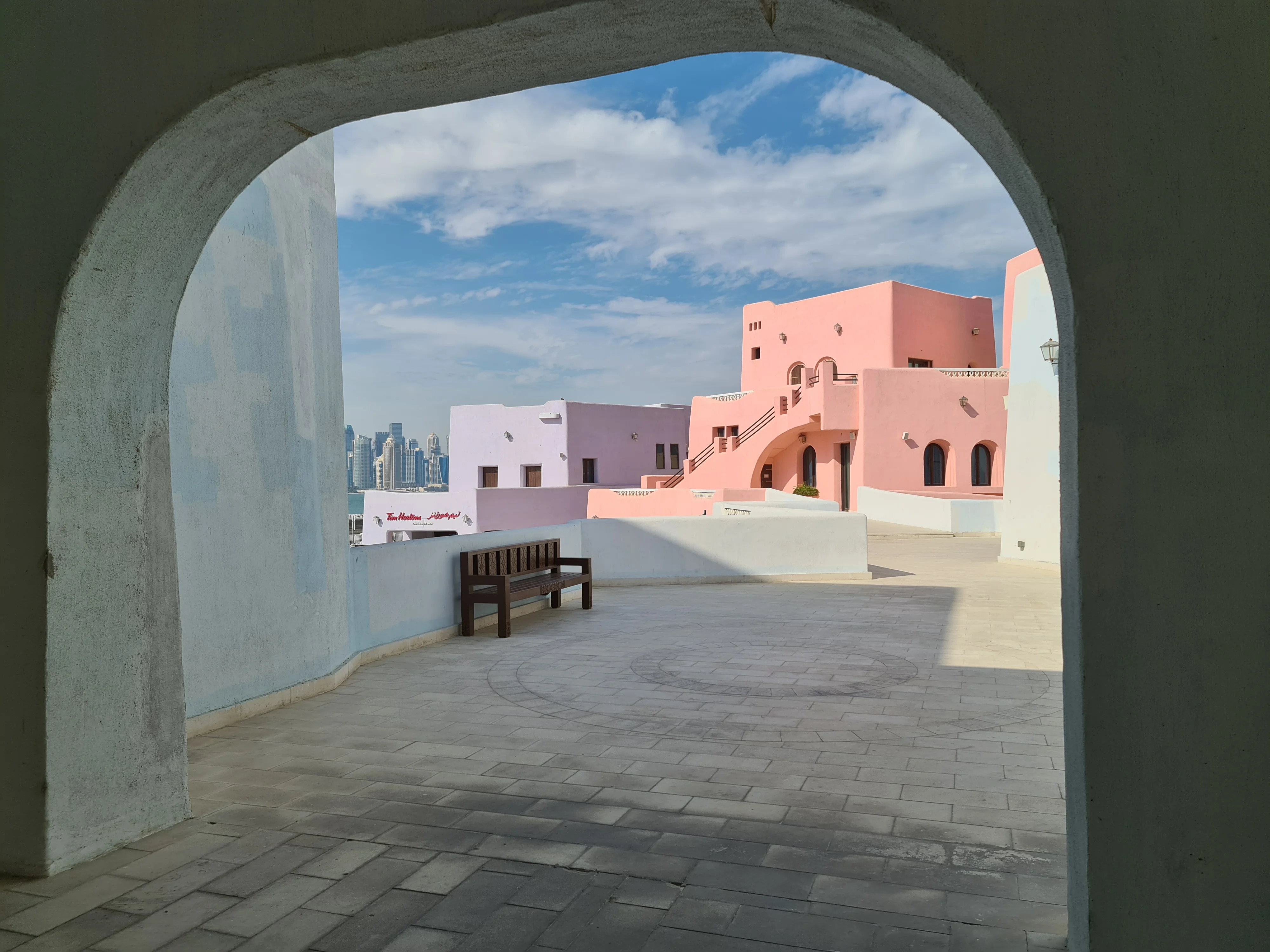 Stone archway framing pastel-coloured buildings in the Mina District, Doha
